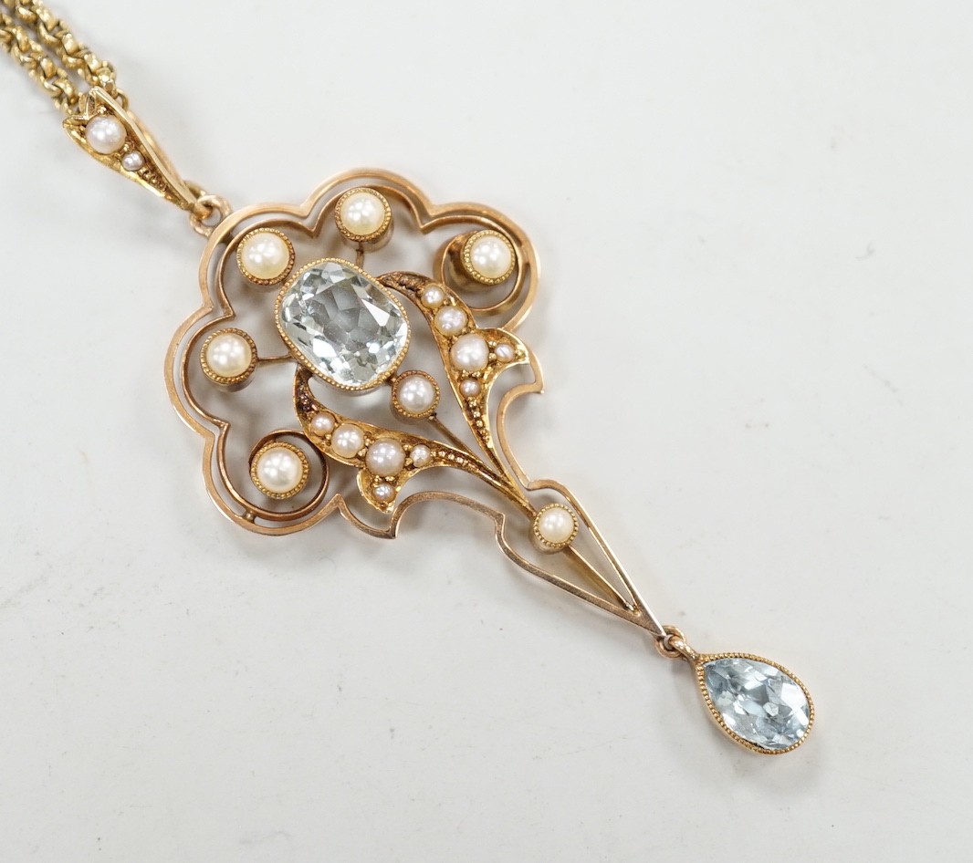 An Edwardian 15ct, aquamarine and seed pearl set drop pendant, 56mm, gross weight 5.3 grams, on a gilt metal chain.